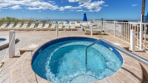 Ein Poolbereich mit Whirlpool, Liegestühlen und Blick auf den Strand.