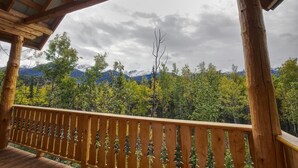 A wooden deck with a railing, overlooking a forested mountain range. - Forget Me Not Cabin (Sutton-Alpine)
