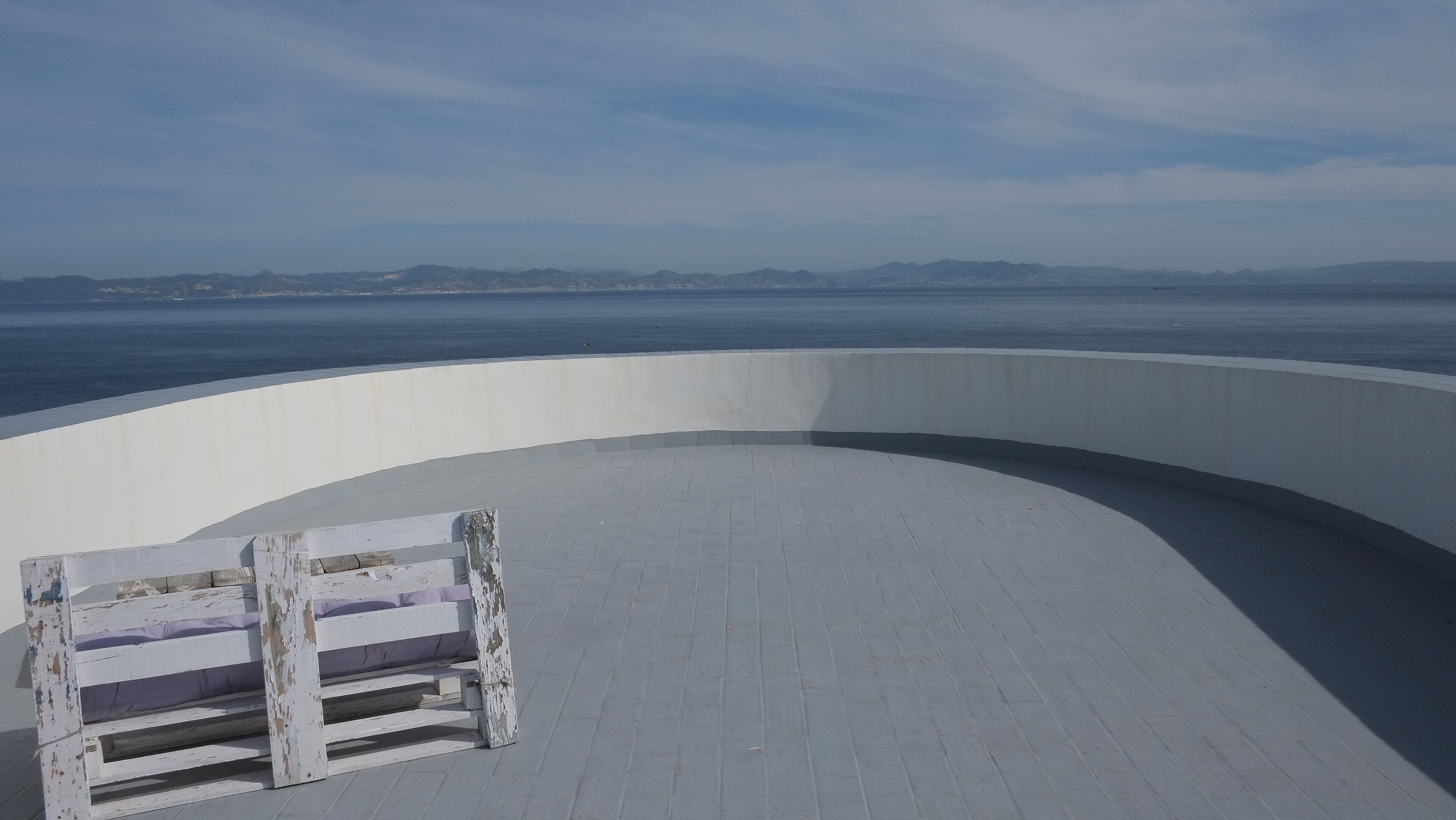 A curved white balcony with a weathered wooden bench.