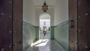 A hallway with a patterned floor, a chandelier, and a view into a room with a large window.