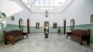 Un grand hall doté d’un haut plafond, de murs décorés de motifs et de deux bancs en bois.