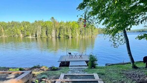 Une terrasse au bord du lac, avec un quai, entourée d’une forêt et sous un ciel dégagé.