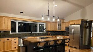 Une cuisine moderne avec des meubles en bois, un réfrigérateur en acier inoxydable et un coin bar équipé de tabourets.
