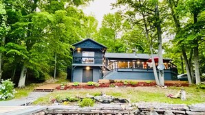 Un chalet au bord du lac, doté d’un quai, entouré d’une végétation luxuriante et d’un mur de pierres.