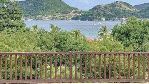 Une vue côtière avec des collines, une étendue d’eau et une clôture en bois au premier plan.