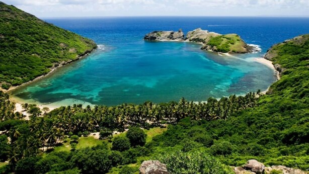 Une plage tropicale aux eaux turquoise et limpides, bordée d’une végétation luxuriante et ponctuée de formations rocheuses.