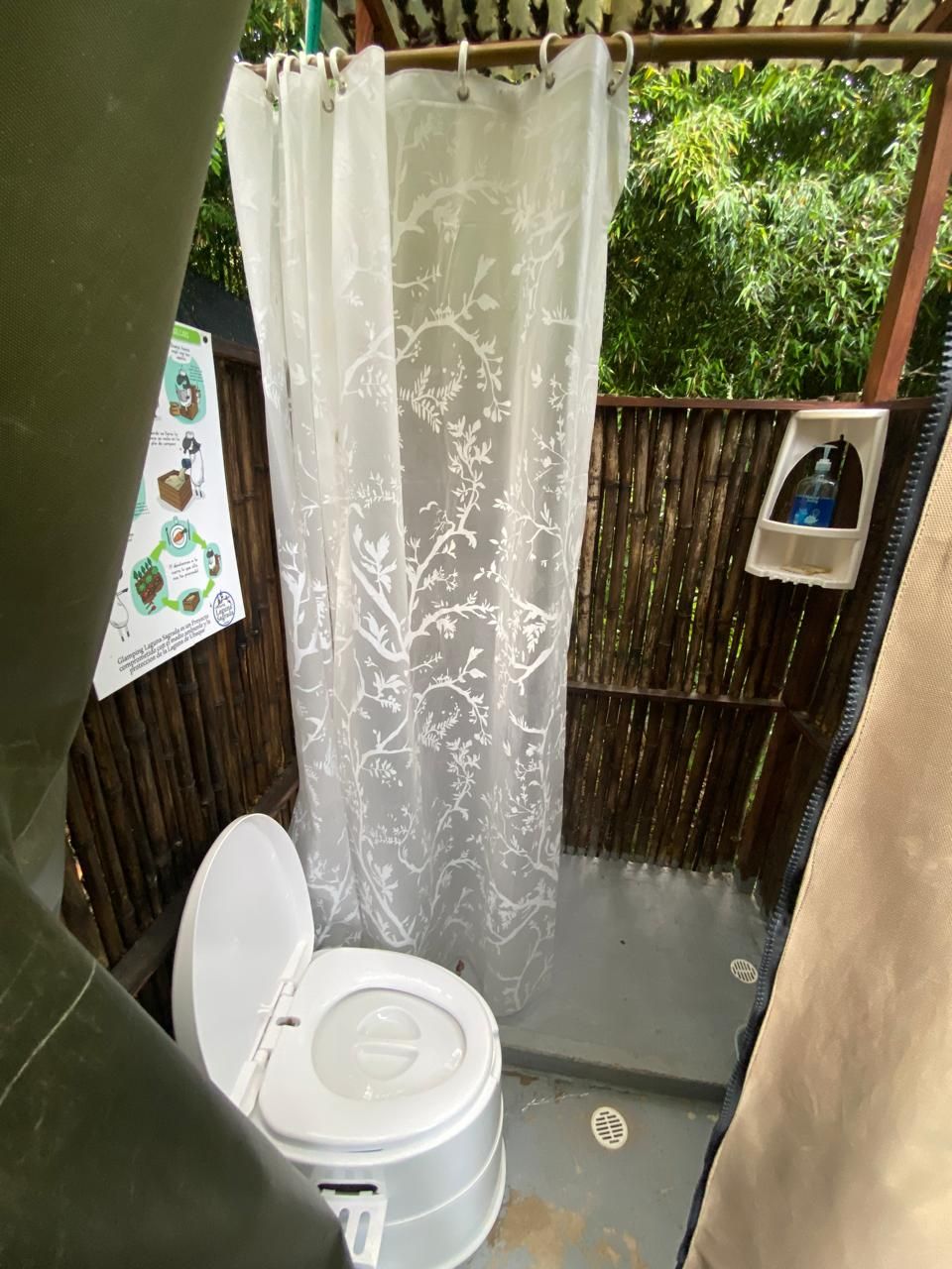 A small, enclosed bathroom with a toilet, a shower curtain with a floral pattern, and a wooden fence outside.