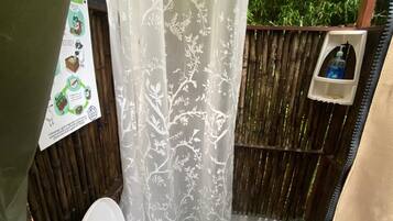 A small, enclosed bathroom with a toilet, a shower curtain with a floral pattern, and a wooden fence outside.
