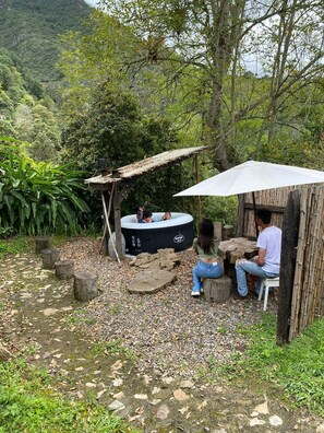 Ein Whirlpool mit Holzkonstruktion und Tisch mit Sonnenschirm in einer natürlichen Umgebung.