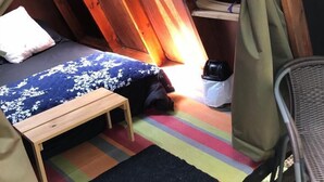 Une chambre mansardée chaleureuse avec un plafond en pente en bois, un lit recouvert d’une couette à motifs floraux, une petite table en bois et un tapis rayé aux couleurs vives.
