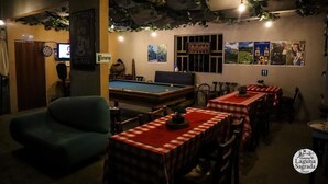 Une pièce chaleureuse avec une table de billard, un jeu de fléchettes et un canapé vert. On y trouve des tables recouvertes de nappes à carreaux rouges et blancs.