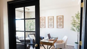 A modern interior with a glass door leading to a living area, a small table with a laptop, and three framed artworks on the wall.