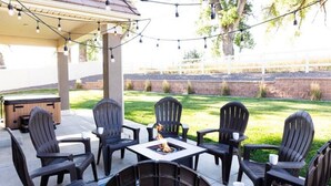 An outdoor patio with four Adirondack chairs, a square table, and a fire pit.