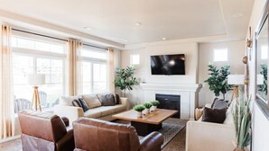 A spacious living room with a fireplace, leather sofas, a coffee table, and large windows.