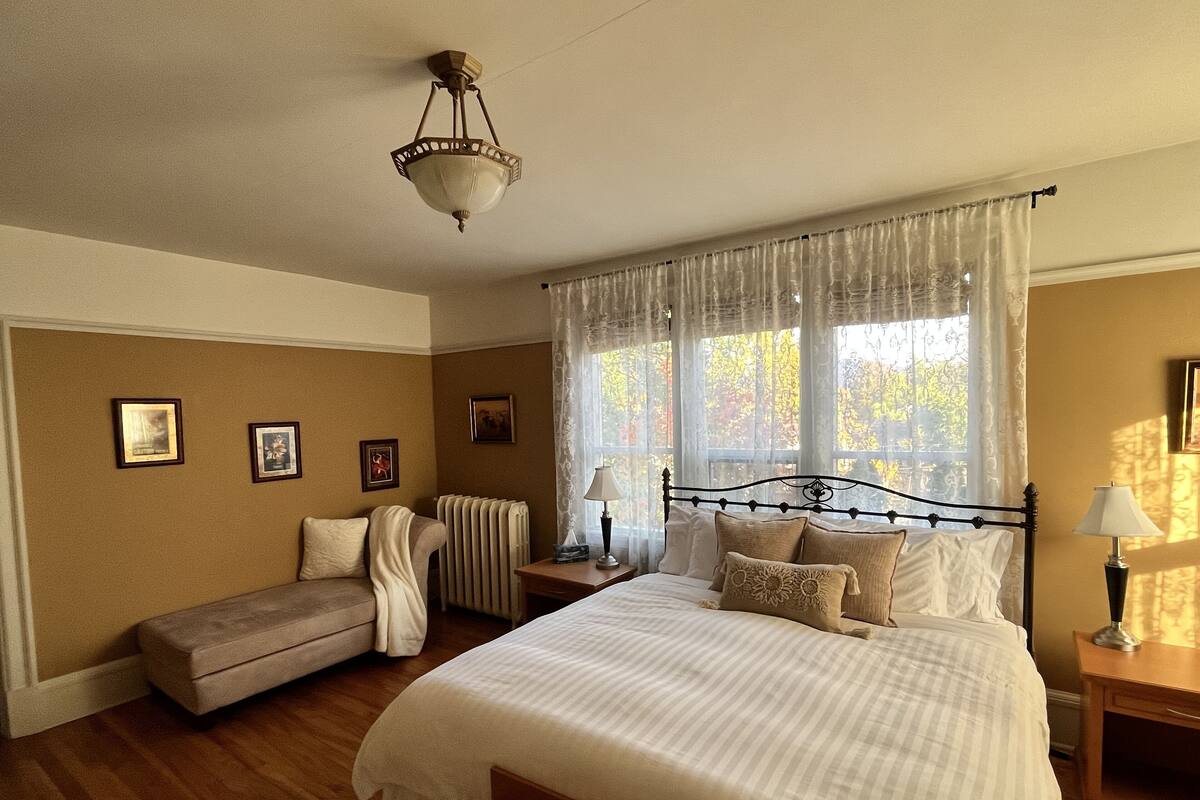 A bedroom with a large bed, a bedside table with lamps, a bench, and a radiator.