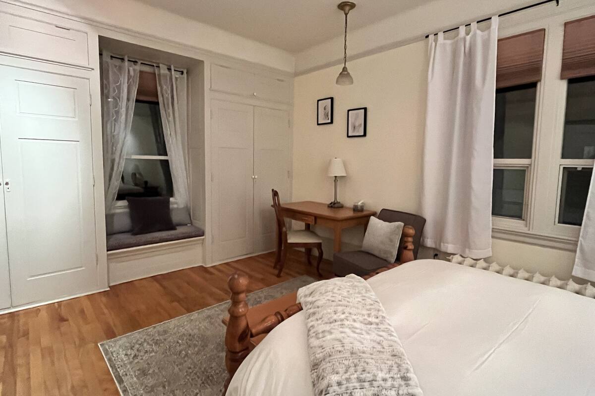 A bedroom with a bed, a desk, a chair, a window with curtains, and a wardrobe.