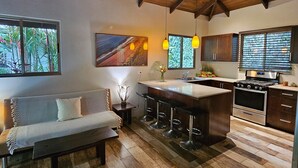 A modern kitchen with a bar area, wooden flooring, and a dining area with a sofa.
