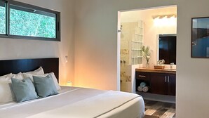 A modern bedroom with a large bed, a nightstand, a bathroom with a glass shower enclosure, and a wooden vanity.