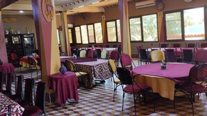 A dining area with multiple tables and chairs, large windows, and a checkered floor. - El Menzeh foundation (Rissani)