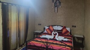 A room with a bed, a wall-mounted picture, and a hanging light fixture. - El Menzeh foundation (Rissani)