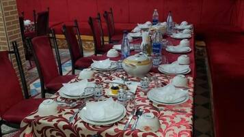 A dining area with a long table set for a meal, surrounded by red upholstered chairs.