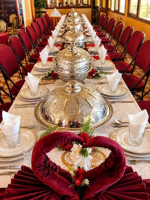 Una larga mesa de comedor dispuesta para una comida formal, con cubertería y cristalería elaborada, organizada de forma simétrica.