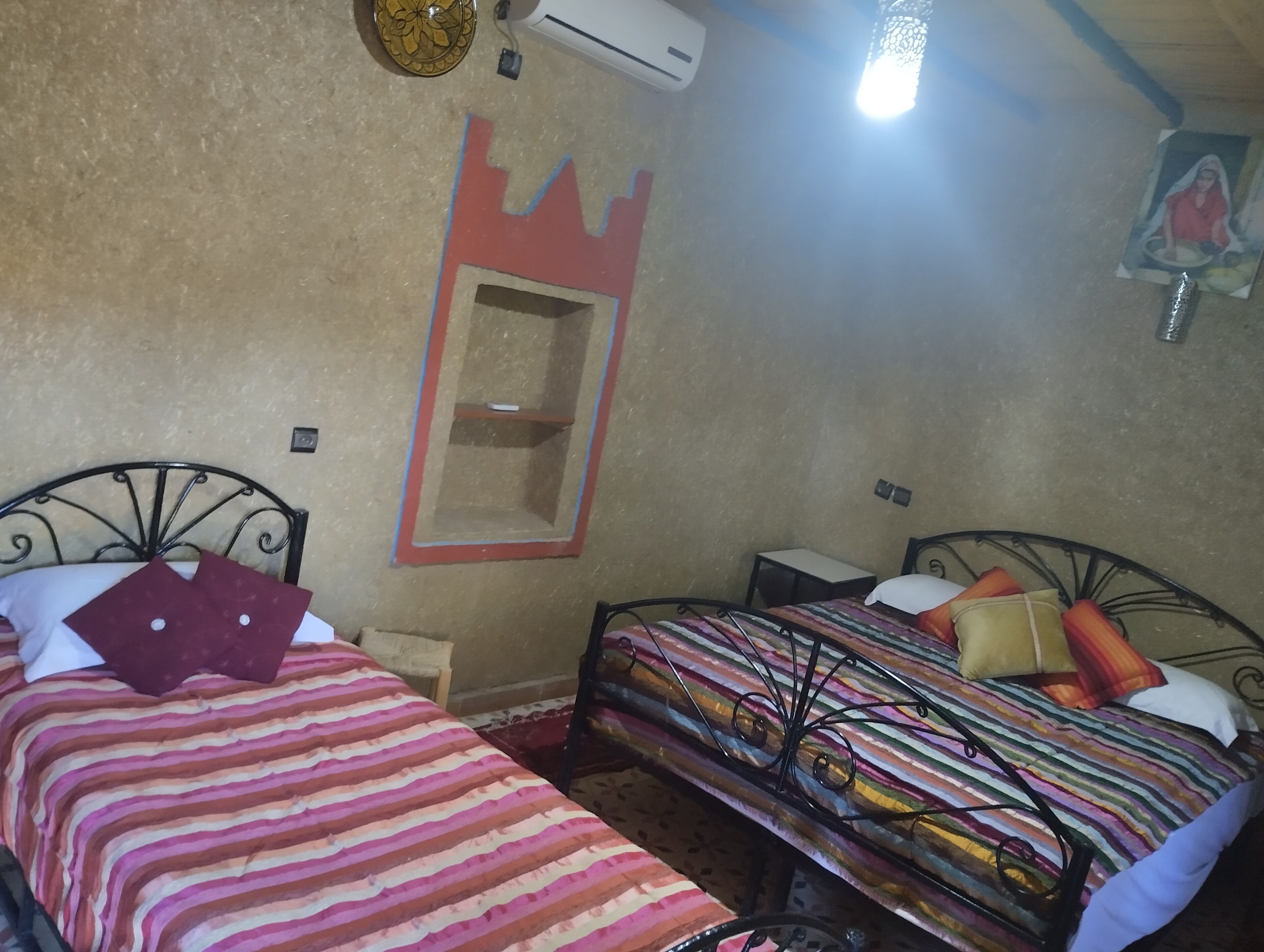 A room with two beds, a small shelf, and a wall-mounted air conditioner.
