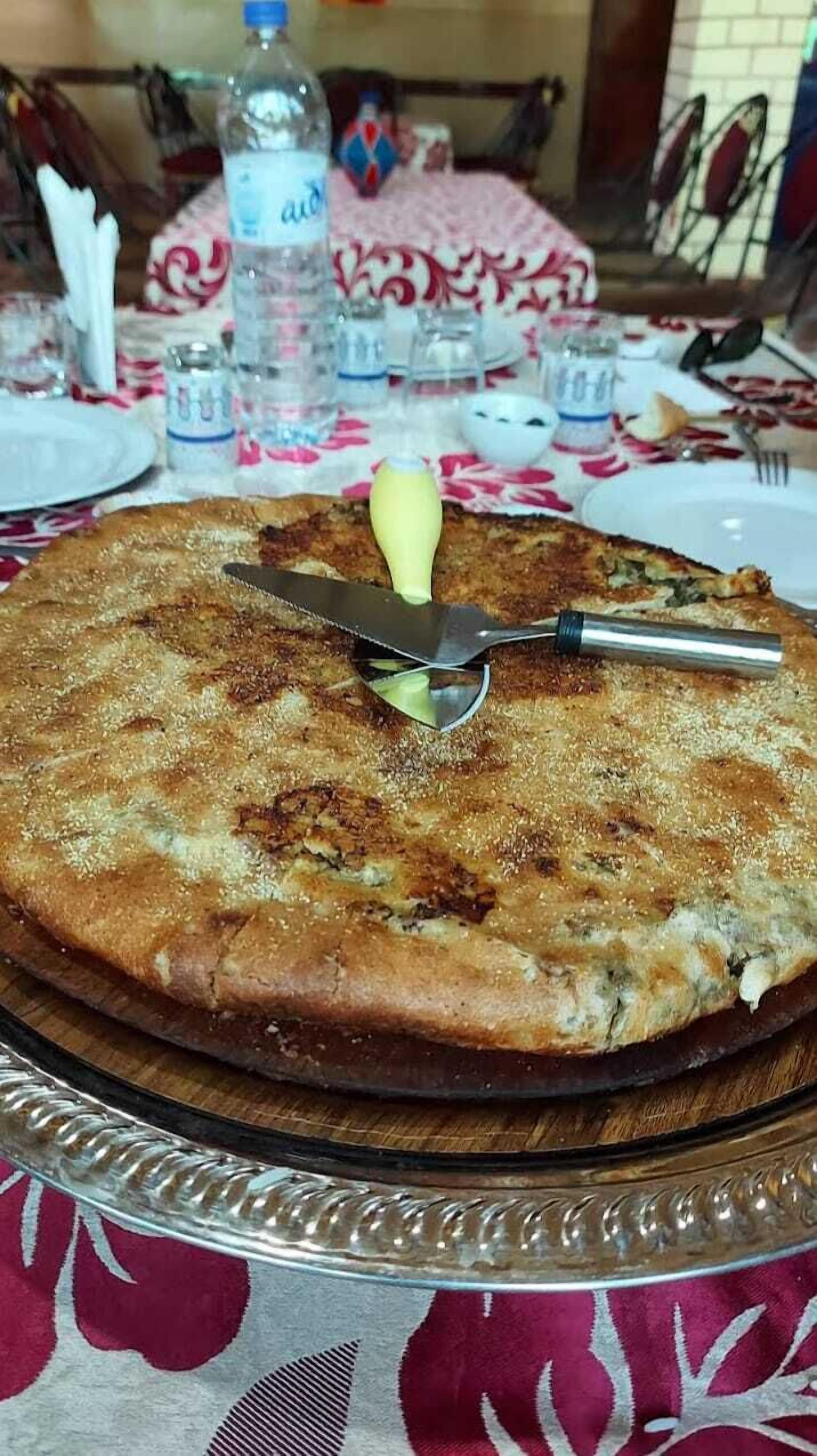 Una pizza redonda sobre una tabla de madera, con un cuchillo y un tenedor encima.