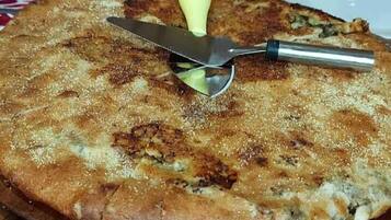 Una pizza redonda sobre una tabla de madera, con un cuchillo y un tenedor encima.