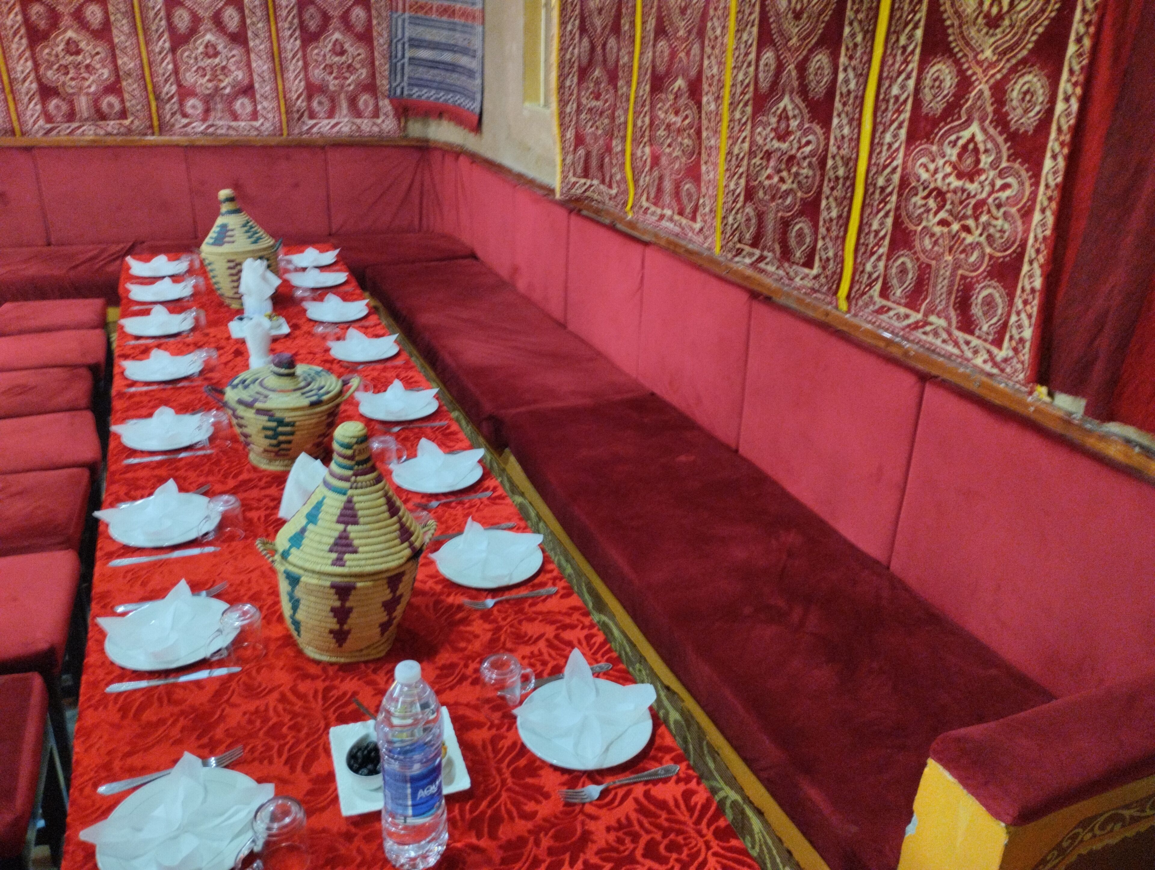 A long dining table set with white plates, cutlery, and decorative vases, surrounded by red upholstered seating.
