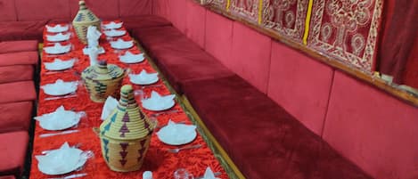 A long dining table set with white plates, cutlery, and decorative vases, surrounded by red upholstered seating.