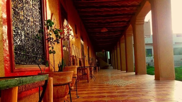 A corridor with tiled flooring, chairs, and a window with decorative ironwork. - El Menzeh foundation (Rissani)