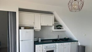 A compact kitchen with white cabinets, a built-in oven, a sink, and a modern pendant light.