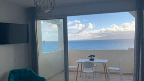 A balcony with a view of the sea, a table with chairs, and a teal chair.