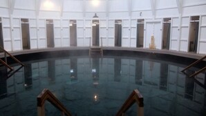 Una amplia piscina interior con una escalera central y varias puertas a lo largo de las paredes.