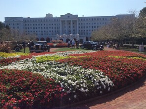 Un edificio con una amplia entrada central, rodeado por un jardín lleno de flores rojas y blancas.