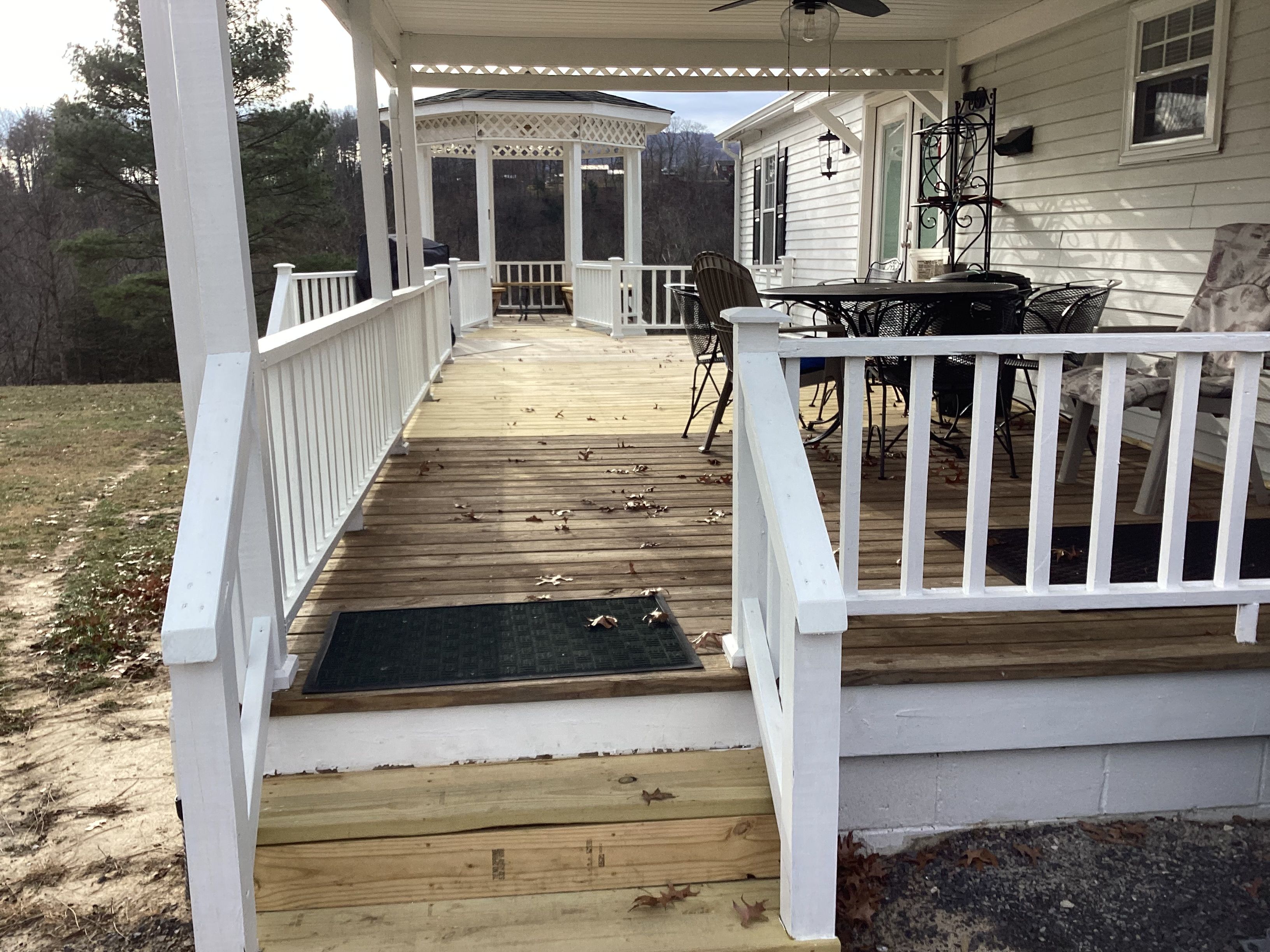 A covered deck with a wooden floor, white railings, and a seating area with chairs and a table.