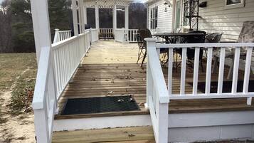 A covered deck with a wooden floor, white railings, and a seating area with chairs and a table.