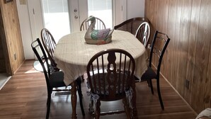 Un comedor con una mesa redonda, seis sillas, un centro de mesa decorativo con forma de cisne, paneles de madera en las paredes y una puerta con persianas.