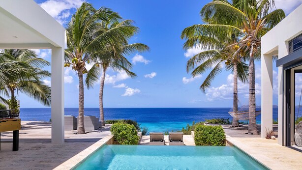 An infinity pool with a view of the ocean, surrounded by palm trees and lounge chairs.