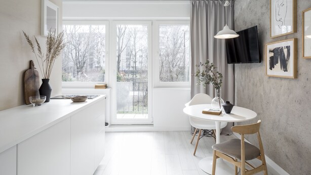 Et moderne køkken med en hvid bordplade, et spiseområde med et rundt bord og stole, og et TV ophængt på væggen.