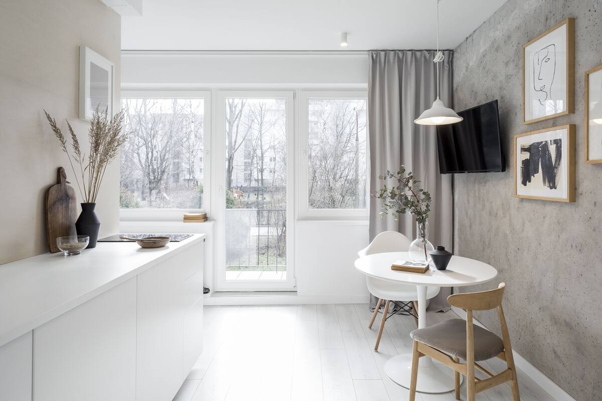 Une cuisine moderne avec un plan de travail blanc, un coin repas avec une table ronde et des chaises, et un téléviseur fixé au mur.