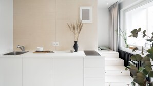 Et moderne køkken med en hvid bordplade, en rustfri stålvask og en sort induktionskogetop. Der står en vase med tørrede planter på bordet.