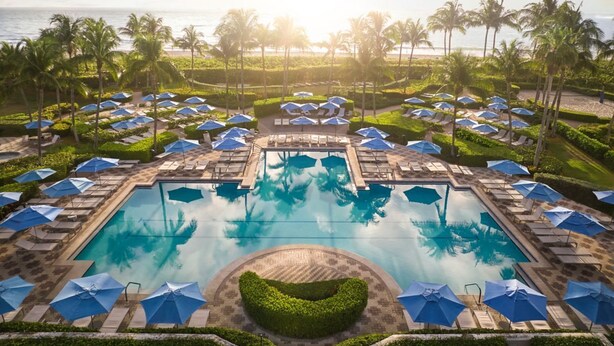 A resort pool area with multiple sun loungers and umbrellas, surrounded by palm trees and a clear view of the ocean. - Beautiful Marriott Ocean Point Resort - Studio Villa - on the beach. (Palm Beach Shores)