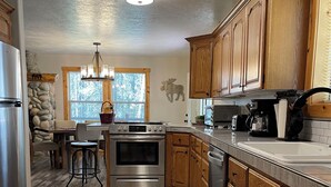 A modern kitchen with wooden cabinets, a built-in oven, a refrigerator, and a dining area with a stone accent wall and a chandelier.