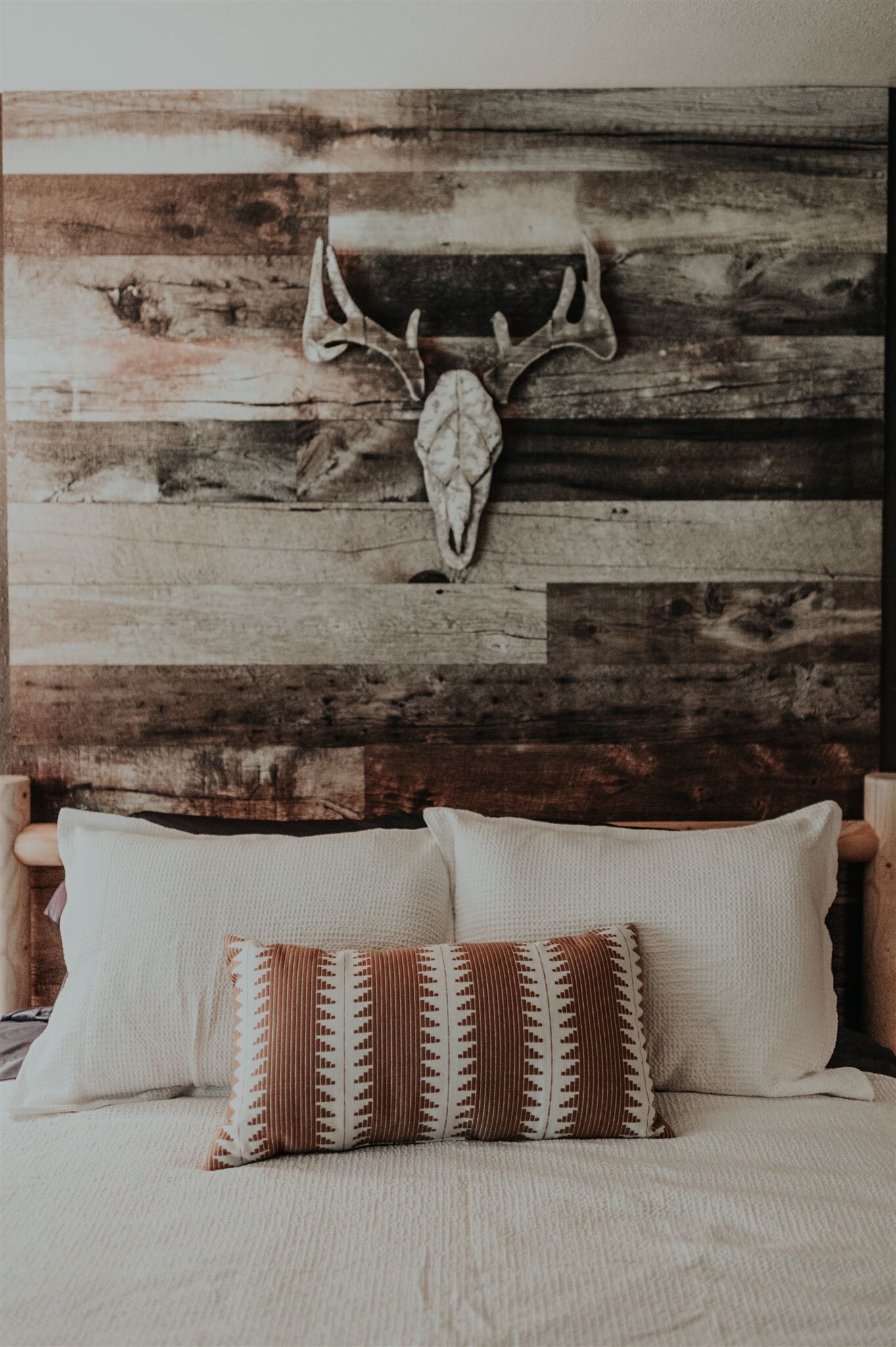 A bed with a wooden headboard, a skull decoration, and patterned pillows.