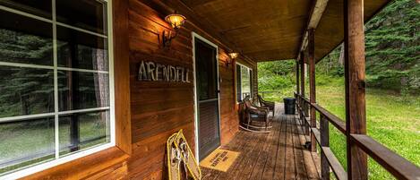 Une cabane en bois avec un porche couvert, une plaque portant le nom « ARENDALL » et un paillasson.