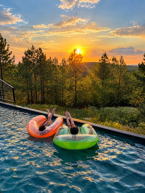 A swimming pool with two inflatable tubes, surrounded by trees and a sunset view.