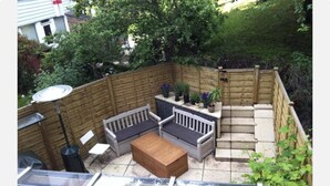 A backyard patio with a wooden fence, a wooden bench, a table, and potted plants. - Modern Bright Shoreditch 2-bed Apartment in London (London)