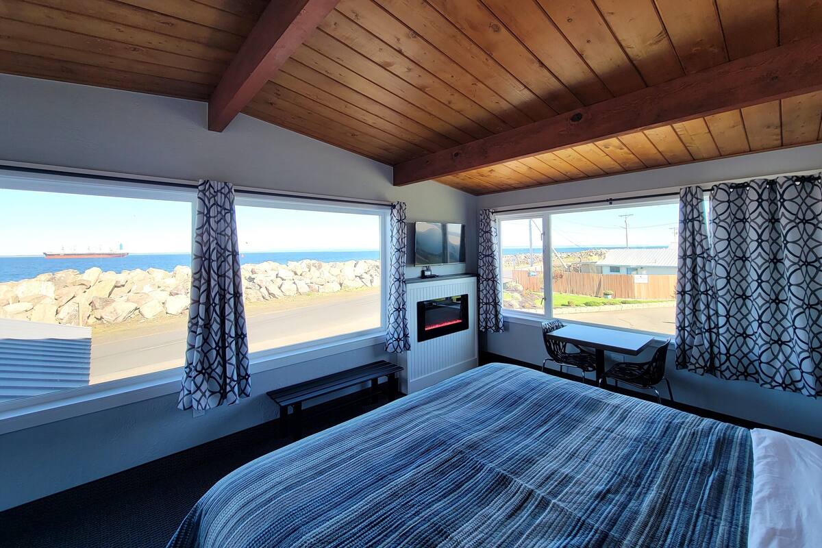 A bedroom with a large bed, a TV, and a view of the sea through a window.